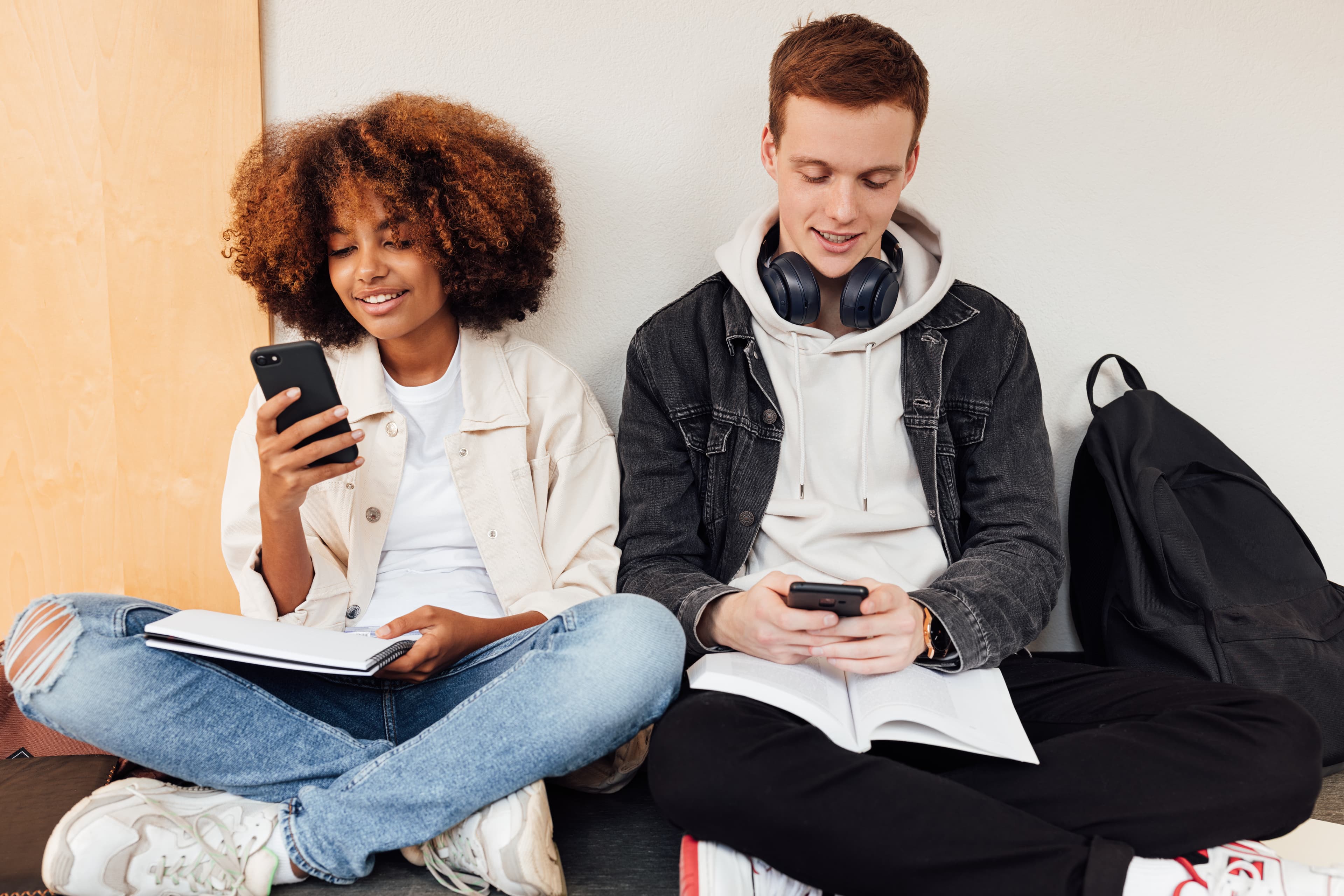 Young woman and man sitting with phones and notebooks.